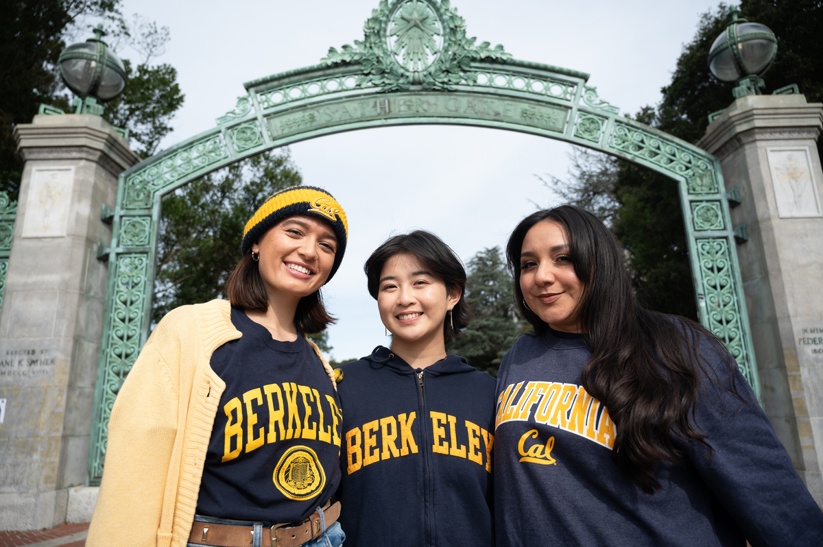Three students wearing Cal gear in front of the Campanile