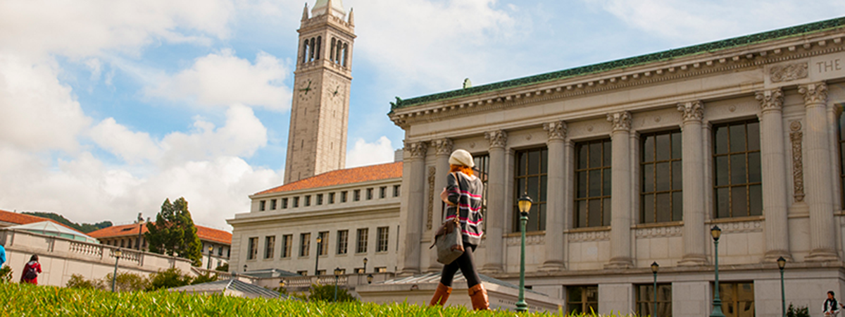 Student walking on the glade in front of doe library and Sather tower in the background